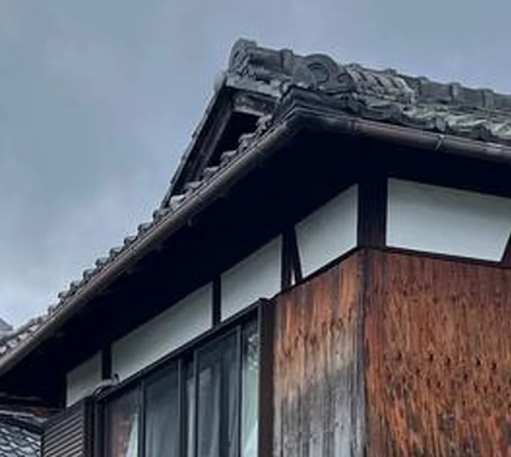 工事前の日本家屋。瓦屋根と白い漆喰壁、板張りの外壁が見える
